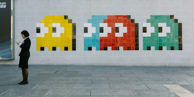 A person looking at their phone stands next to four differently coloured space invader characters of a wall