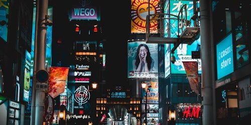 A cityscape of billboards showing different adverts above the heads of a crowd of shoppers