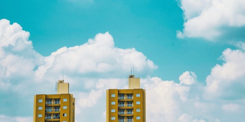 The tops of two yellow tower blocks stand before clouds in a blue sky