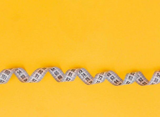 A twisted tape measure against a yellow background