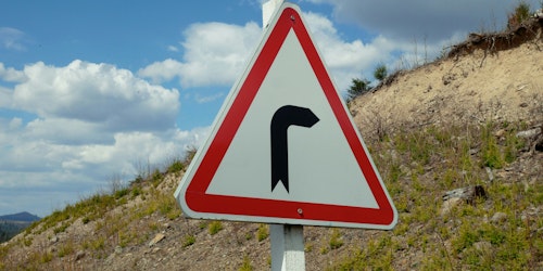 A white arrow with an angle bend in it is painted onto a grey paved raod 