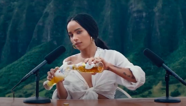 Zoe Kravitz pours a Michelob beer into a glass in front of two microphones in a still from a Super Bowl ad for the beer