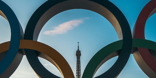 The Eiffel Tower is visible through one of the Olympic rings