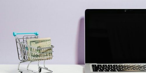 A shopping trolley containing bank notes next to a laptop, representing omnichannel customer service in the retail sector