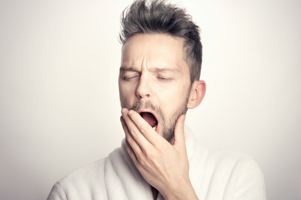 A man in a light-colored shirt raises his hand to his mouth as he yawns